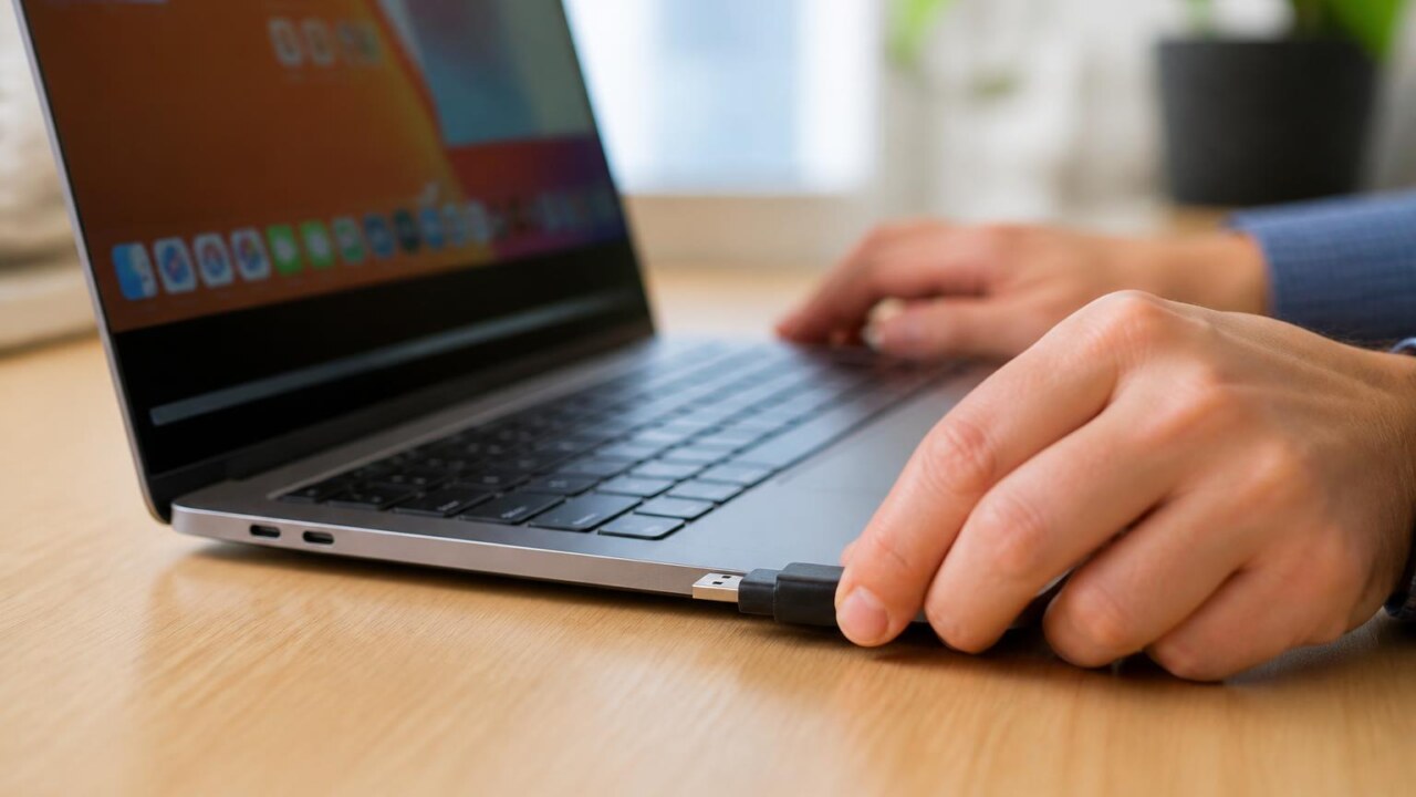 Mãos conectando um pendrive em um laptop com tela mostrando ícones de aplicativos
