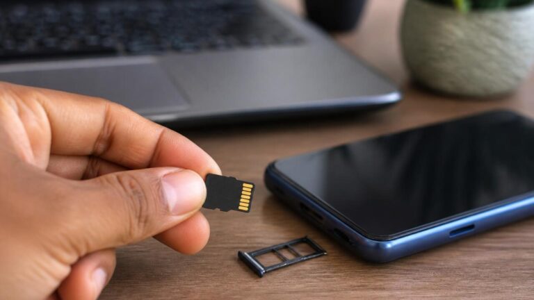 Cartão microSD ao lado de um celular com gaveta de chip aberta, representando compatibilidade de armazenamento.