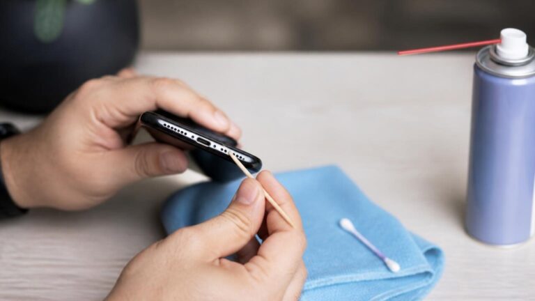 Pessoa limpando a porta de carregamento de um celular com palito de madeira e microfibra