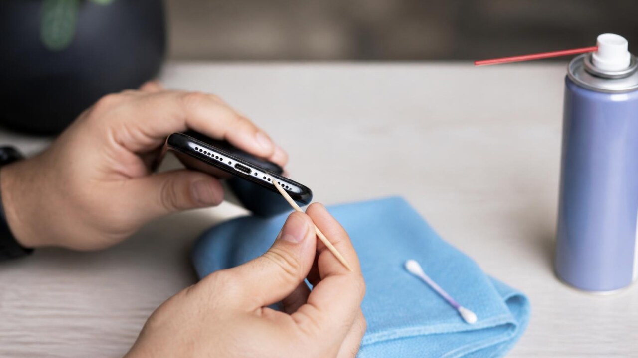 Pessoa limpando a porta de carregamento de um celular com palito de madeira e microfibra