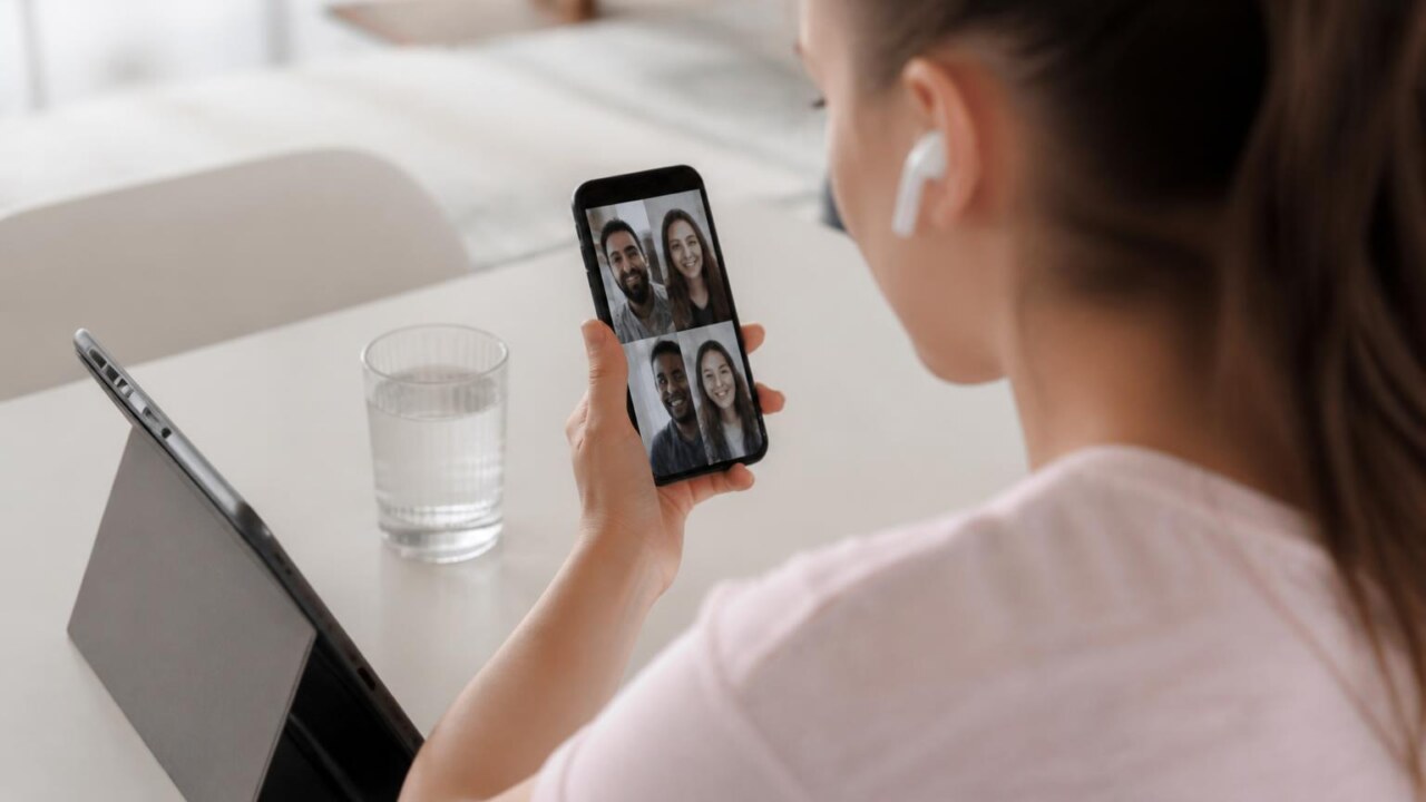 Pessoa segurando smartphone em chamada de vídeo com vídeo conferência na tela