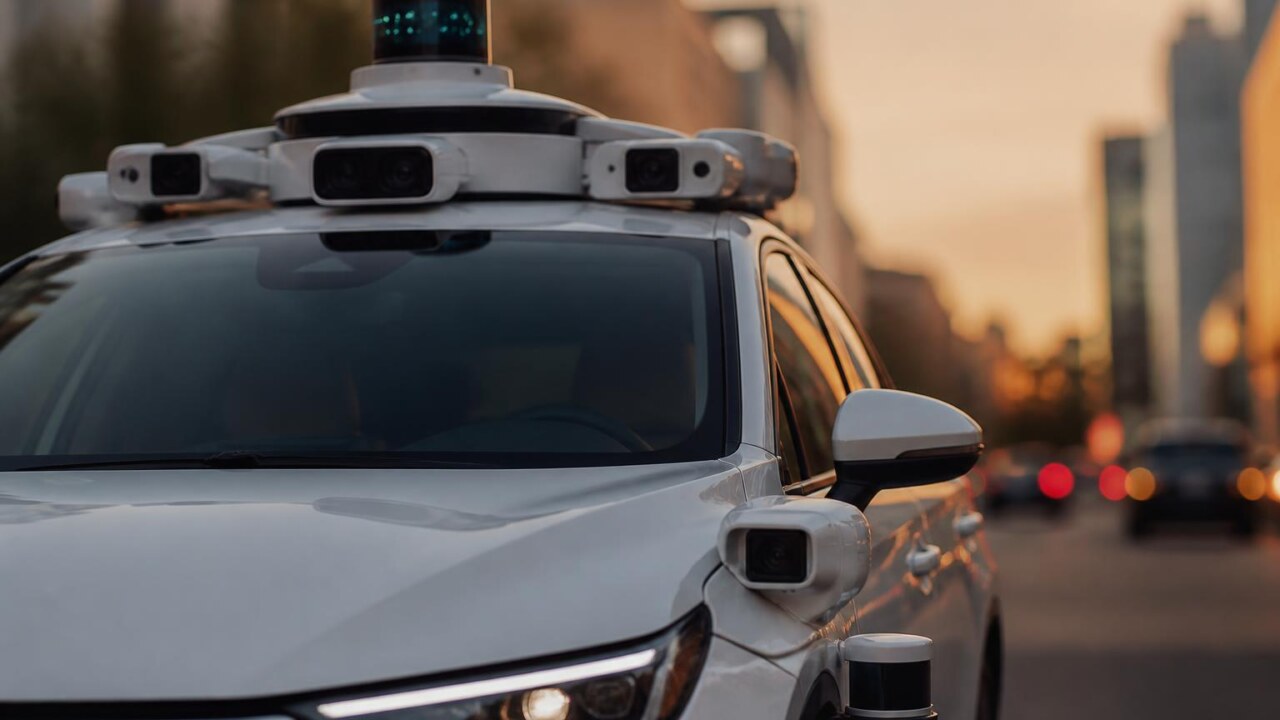Veículo autônomo equipado com sensores como LiDAR, câmeras e radar em estrada urbana ao entardecer.
